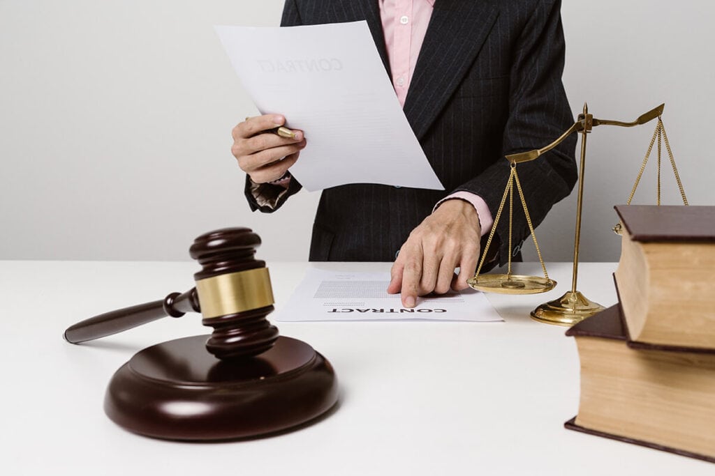 Lawyer reading a legally binding contract with a gavel, weights of justice and books on the desk.