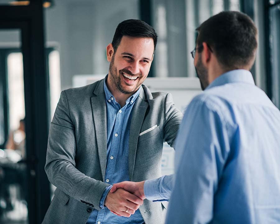 Two clients in business attire smiling and shaking hands.