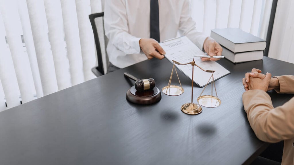 Lawyer and client having a consultation with a scales of justice in front of them on table.